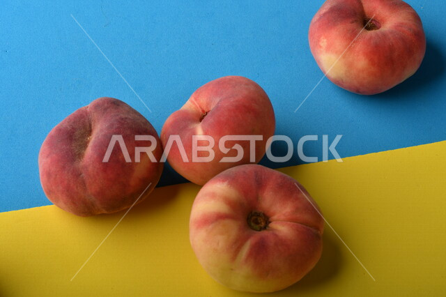 صورة لفاكهة الخوخ المسطح اللذيذ على خلفية ملونة باللونين الأصفر والأزرق ، ثمرة الدّراق الصحية اللذيذة ، فاكهة الدُّراق المُبلَّط وتسمى كعب الغزال ، فاكهة صيفية