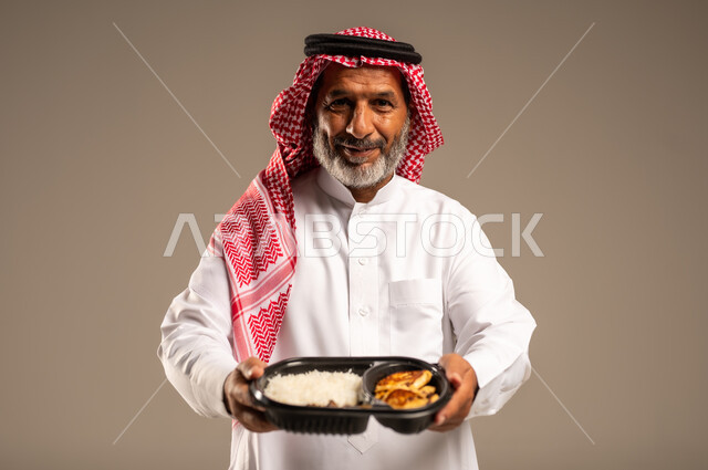 مبادرات وتبرعات انسانية خيرية، الاستمتاع بتناول الوجبات السريعة, بورتريه مقرب لرجل كبير السن عربي خليجي سعودي مبتسم يرتدي الشماغ والثوب التقليدي يمسك بيده وجبة طعام ينظر الى الكاميرا بإيماءات السرور، توفير الغذاء للمحتاجين، خلفية بيج