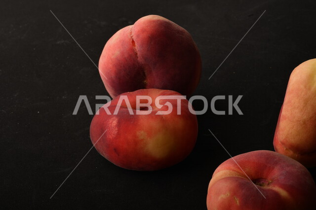 صورة لفاكهة الخوخ المسطح اللذيذ على خلفية سوداء ، ثمرة الدّراق الصحية اللذيذة ، فاكهة الدُّراق المُبلَّط وتسمى كعب الغزال ، فاكهة صيفية