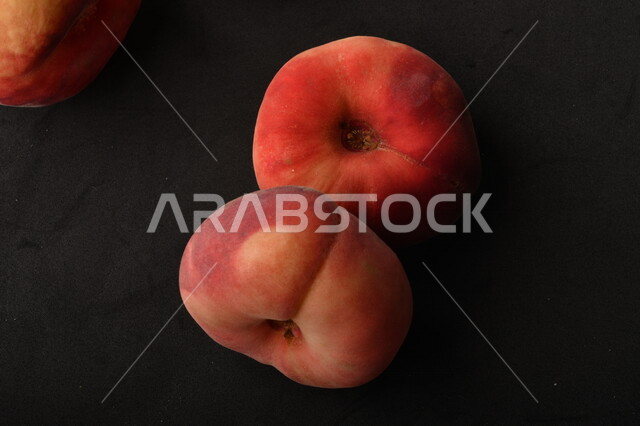 صورة لفاكهة الخوخ المسطح اللذيذ على خلفية سوداء ، ثمرة الدّراق الصحية اللذيذة ، فاكهة الدُّراق المُبلَّط وتسمى كعب الغزال ، فاكهة صيفية