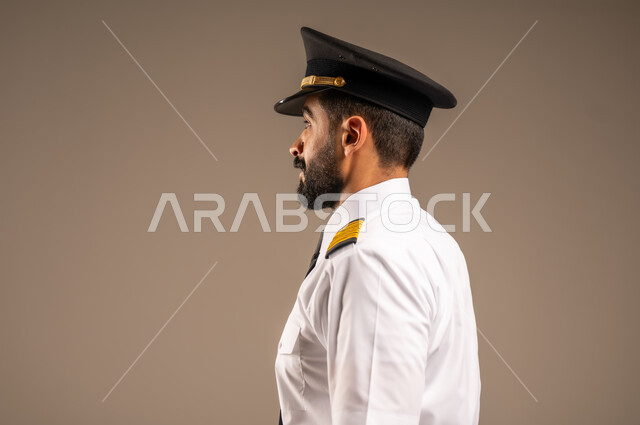  طاقم الاستقبال والترحيب بالركاب، العمل في مجال الطيران، مفهوم السياحة والسفر، رحلات جوية سياحية, خطوط الطيران السعودية,  بورتريه لكابتن طيار عربي سعودي خليجي مبتسم يرتدي الزي الرسمي يقف باستقامة ينظر الى الكاميرا بتعابير السعادة والسرور، خلفية ملونة