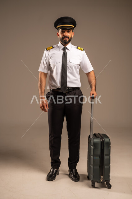 العمل في مجال الطيران، طاقم الاستقبال والترحيب بالركاب، مفهوم السياحة والسفر، رحلات جوية سياحية, خطوط الطيران السعودية,  بورتريه لكابتن طيار عربي سعودي خليجي مبتسم يرتدي الزي الرسمي يجر حقيبة سوداء، خلفية ملونة