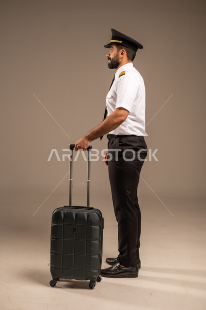 العمل في مجال الطيران، طاقم الاستقبال والترحيب بالركاب، مفهوم السياحة والسفر، رحلات جوية سياحية, خطوط الطيران السعودية,  بورتريه لكابتن طيار عربي سعودي خليجي مبتسم يرتدي الزي الرسمي يجر حقيبة سوداء، خلفية ملونة