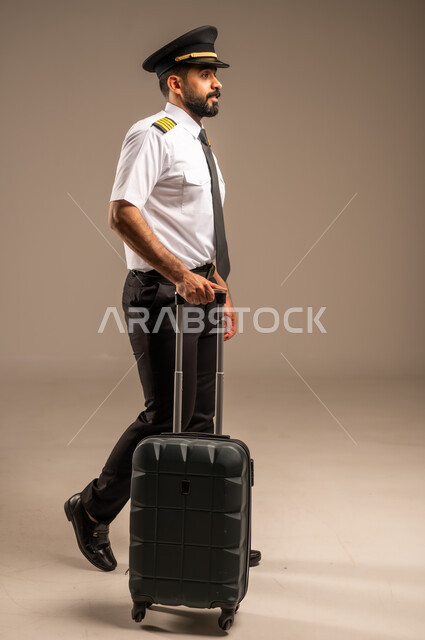 Aviation work, passenger reception and welcome crew, tourism and travel concept, tourist flights, Saudi Airlines, portrait of a smiling Saudi Arabian Gulf captain in uniform pulling a black bag, colorful background