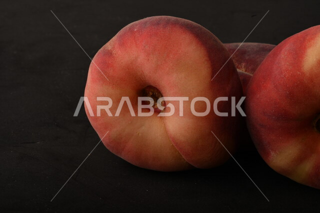 صورة لفاكهة الخوخ المسطح اللذيذ على خلفية سوداء ، ثمرة الدّراق الصحية اللذيذة ، فاكهة الدُّراق المُبلَّط وتسمى كعب الغزال ، فاكهة صيفية