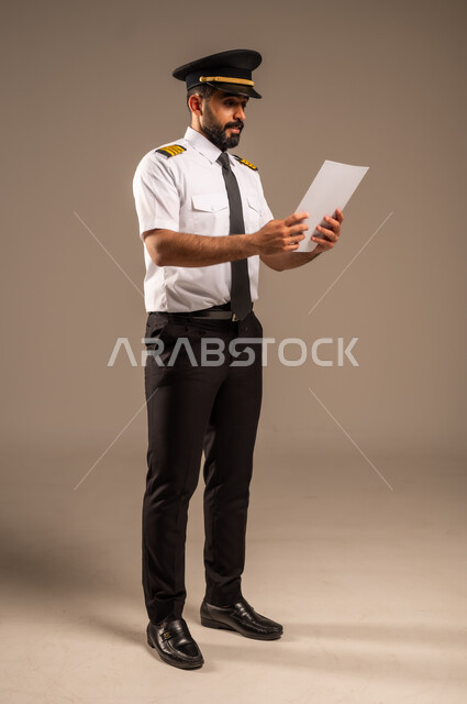 القاء ارشادات السلامة على المسافرين، العمل في مجال الطيران، طاقم الاستقبال والترحيب بالركاب، مفهوم السياحة والسفر، رحلات جوية سياحية, خطوط الطيران السعودية,  بورتريه لكابتن طيار عربي سعودي خليجي مبتسم يرتدي الزي الرسمي يحمل بيده ورقة بيضاء فارغة، خلفية ملونة