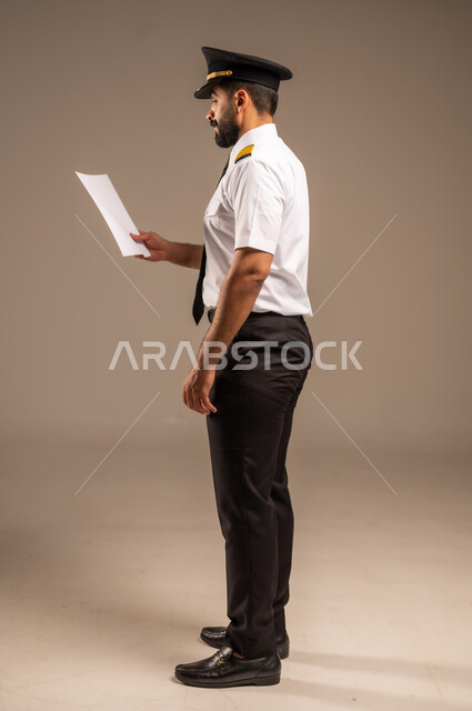 القاء ارشادات السلامة على المسافرين، العمل في مجال الطيران، طاقم الاستقبال والترحيب بالركاب، مفهوم السياحة والسفر، رحلات جوية سياحية, خطوط الطيران السعودية,  بورتريه لكابتن طيار عربي سعودي خليجي مبتسم يرتدي الزي الرسمي يحمل بيده ورقة بيضاء فارغة، خلفية ملونة