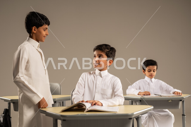 المشاركة والتعاون بين الزملاء، جودة أساليب التعلم الفعال، موسم العودة إلى المدارس، بورتريه لطلاب عربيين خليجيين سعوديين يرتدون الزي المدرسي يجلسون في مقاعدهم وأمامهم الكتب والمقررات المدرسية، أهداف التربية والتعليم في المملكة العربية السعودية، خلفية رمادية