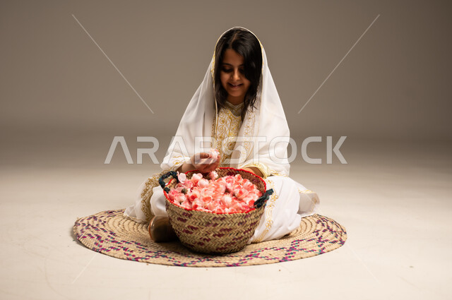 Anniversary of the founding of the Saudi state February 22, fragrant flowers and roses, old popular handicrafts and crafts, close-up portrait of a smiling Saudi Arabian Gulf girl wearing a shayla and a narshel, holding natural roses in her hand, sitting on a straw rug, wearing the costumes of the Eastern Province, the day we started 1727 AD, beige background