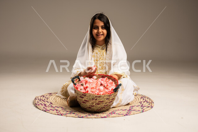 Anniversary of the founding of the Saudi state February 22, fragrant flowers and roses, old popular handicrafts and crafts, close-up portrait of a smiling Saudi Arabian Gulf girl wearing a shayla and a narshel, holding natural roses in her hand, sitting on a straw rug, wearing the costumes of the Eastern Province, the day we started 1727 AD, beige background