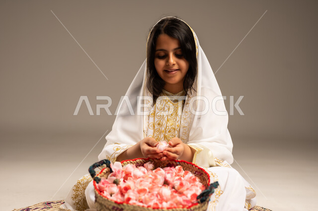 ذكرى تاسيس الدولة السعودية 22فبراير، الزهور والورود العطرية، حرف ومهن يدوية شعبية قديمة، بورتريه مقرب لفتاة عربية خليجية سعودية مبتسمة ترتدي الشيلة والنشل تحمل بيدها الورد الجوري الطبيعي، الجلوس على سجادة مصنوعة من القش، ارتداء أزياء المنطقة الشرقية، يوم بدينا1727م، خلفية بيج 