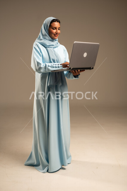 ادارة الأعمال عن بعد، استخدام الأجهزة الحديثة والمتطورة، بورتريه لامرأة عربية خليجية سعودية ترتدي العباءة والحجاب تقوم باستخدام الحاسوب المحمول، دمج التكنولوجيا بالعمل، إنجاز المهام المطلوبة عبر اللابتوب، مهن ووظائف نسائية، خلفية ملونة