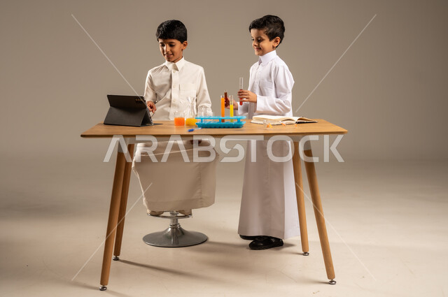 العمل الجماعي والتعاون بين الزملاء، الاستفادة من التقنيات والأجهزة التكنولوجية بالتعلم الفعال، استخدام الأدوات والوسائل التعليمية التجريبية، بورتريه لطالبين عربيين خليجيين سعوديين يرتديان الزي المدرسي يقومان بإجراء التجارب والاختبارات الكيميائية، خلفية رمادية