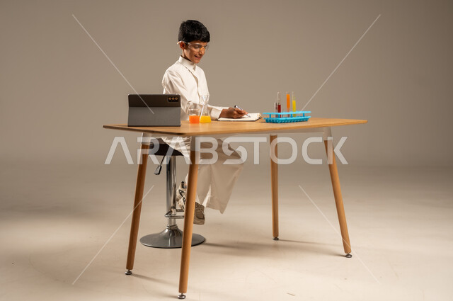 Utilizing modern technological techniques and devices for effective learning, using experimental educational tools and means, portrait of a Saudi Arabian Gulf student wearing school uniform and safety glasses sitting behind an examination table and sample tubes and chemical analyses, gray background
