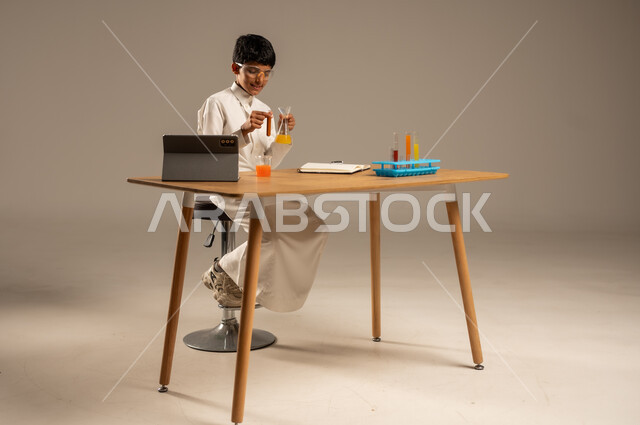 Utilizing modern technological techniques and devices for effective learning, using experimental educational tools and means, portrait of a Saudi Arabian Gulf student wearing school uniform and safety glasses sitting behind an examination table and sample tubes and chemical analyses, gray background