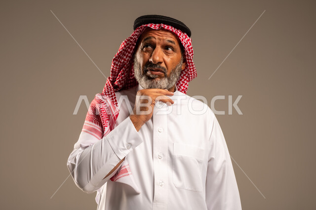  التقدم بالعمر والهيبة،  النظر الى شيء ما، بورتريه لرجل كبير بالسن عربي خليجي سعودي يرتدي الثوب التقليدي و الشماغ, الاهتمام بالأناقة والمظهر الخارجي، الوقوف باستقامة وثبات، مفهوم الرجولة العربية، خلفية بيج