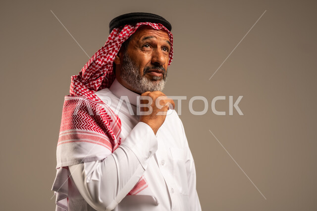  التقدم بالعمر والهيبة،  النظر الى شيء ما، بورتريه لرجل كبير بالسن عربي خليجي سعودي يرتدي الثوب التقليدي و الشماغ, الاهتمام بالأناقة والمظهر الخارجي، الوقوف باستقامة وثبات، مفهوم الرجولة العربية، خلفية بيج