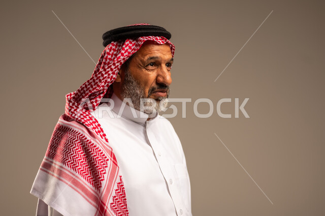  التقدم بالعمر والهيبة،  النظر الى شيء ما، بورتريه لرجل كبير بالسن عربي خليجي سعودي يرتدي الثوب التقليدي و الشماغ, الاهتمام بالأناقة والمظهر الخارجي، الوقوف باستقامة وثبات، مفهوم الرجولة العربية، خلفية بيج