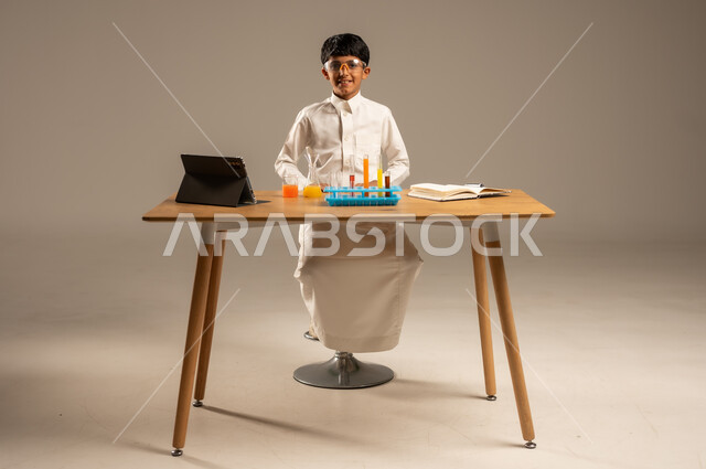 Effective learning methods using technology and technological devices, using experimental educational tools and means, portrait of a Saudi Arabian Gulf student wearing school uniform and safety glasses sitting behind an examination table and sample tubes and chemical analyses, gray background