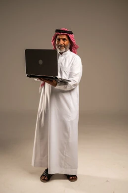 Using laptop to complete tasks, portrait of elderly Saudi Arabian Gulf man wearing traditional keffiyeh and thobe holding laptop looking at camera with gestures of pleasure, development of technology and modern techniques, remote business meeting, full body image, beige background