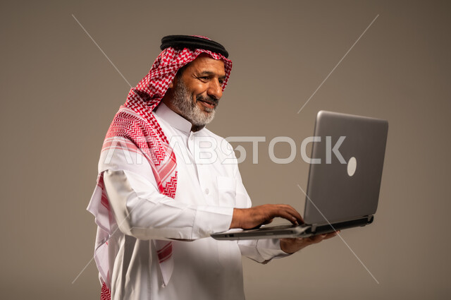 Development of technology and modern techniques, using laptop to accomplish tasks, close-up portrait of elderly Saudi Arabian Gulf man wearing traditional keffiyeh and thobe holding laptop, remote business meeting, online video calls, beige background