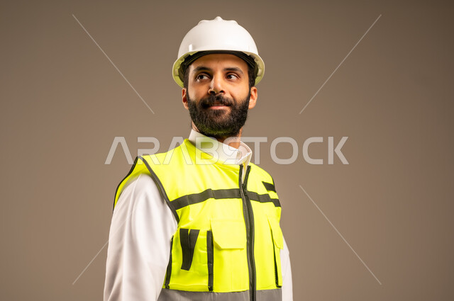 مهن ووظائف سعودية للشباب، مفهوم الهندسة والانشاءات المعمارية، بورتريه مقرب لمهندس عربي خليجي سعودي يرتدي الثوب التقليدي والسترة الخاصة وخوذة الحماية ينظر إلى شيء ما يقوم بمتابعة الأعمال، الإعمار بسواعد أبناء الوطن، خلفية بيج
