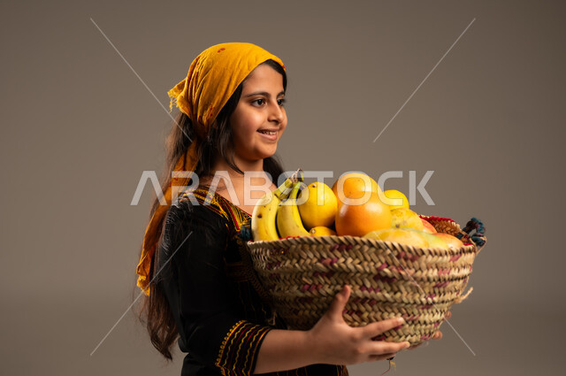 منتجات ومحاصيل زراعية وطنية، ذكرى تأسيس الدولة السعودية 22 فبراير، يوم بدينا 1727م، ارتداء أزياء المنطقة الجنوبية، بورتريه مقرب من الجانب لفتاة عربية خليجية سعودية ترتدي الشيلة والسدرة تحمل بيدها سلة مصنوعة من القش مليئة بالفواكه الطازجة، خلفية بيج
