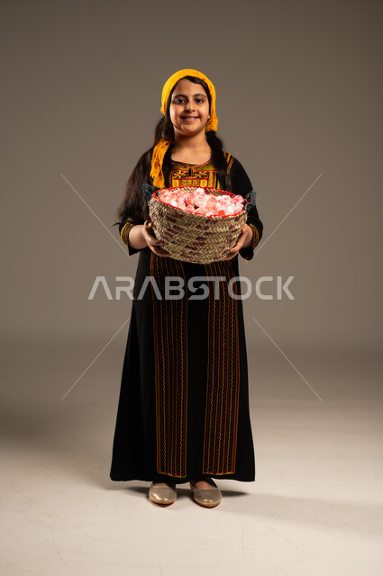 الزهور والورود العطرية، يوم بدينا1727م، بورتريه مقرب لفتاة عربية خليجية سعودية مبتسمة ترتدي الشيلة والسدره تحمل بيدها سلة قش ممتلئة بالورد الجوري الطبيعي، ارتداء أزياء المنطقة الجنوبية، ذكرى تاسيس الدولة السعودية 22فبراير، تعابير الفخر والاعتزاز، الجسم الكامل بالطول، خلفية بيج 