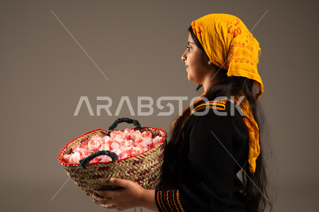 Flowers and fragrant roses, the day we started 1727 AD, a close-up portrait from the back of a Saudi Arabian Gulf girl wearing a shayla and a sidr tree, holding a straw basket full of natural roses, wearing the costumes of the southern region, old popular professions and handicrafts, the anniversary of the founding of the Saudi state, February 22, beige background