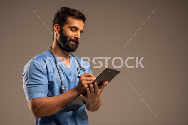 حسن التعامل مع المراجعين، إعداد التقارير وتقديم الخدمات الصحية، بورتريه مقرب لممرض عربي خليجي سعودي يرتدي اليونيفورم يضع السماعة الطبية حول عنقه يحمل بيده ملفات المرضى، العمل في القطاع الصحي في المملكة العربية السعودية، خلفية بيج