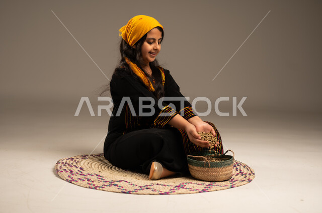 الجلوس على حصيرة مصنوعة من القش، منتجات ومحاصيل محلية وطنية سعودية، ذكرى تأسيس الدولة السعودية الأولى 22 فبراير، يوم بدينا 1727 م، بورتريه مقرب لفتاة عربية خليجية سعودية مبتسمة ترتدي الشيلة والسدره تقوم بوضع الحبوب في السلة، ، ارتداء أزياء المنطقة الجنوبية، مهن وحرف يدوية شعبية قديمة، خلفية بيج