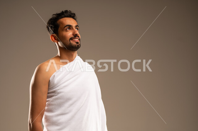 زيارة البيت الحرام في مكة المكرمة، مفهوم العبادة والتقرب الى الله بالاعمال الصالحه، بورتريه مقرب لرجل مسلم عربي خليجي سعودي مبتسم يرتدي ثوب الاحرام بإستعداد لأداء مناسك فريضة الحج والعمرة، الركن الخامس من أركان الاسلام لمن استطاع اليه سبيلا، ايماءات السعادة والطمأنينة، خلفيه بيج