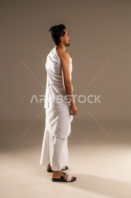 زيارة البيت الحرام في مكة المكرمة، مفهوم العبادة والتقرب الى الله، بورتريه مقرب من الخلف لرجل عربي خليجي سعودي يرتدي ثوب الاحرام ينظر الى مكان ما، أداء مناسك الحج والعمرة، الركن الخامس من أركان الاسلام لمن استطاع اليه سبيلا، الجسم الكامل بالطول، خلفيه بيج