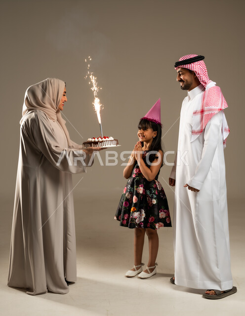 ايماءات البهجة والسرور, الاجتماعات والاحتفالات العائلية، بورتريه لعائلة عربية خليجية سعودية يحتفلون بعيد ميلاد طفلتهم ويقدمون لها قالب الكيك المزين، الألفة والمودة بين أفراد الأسرة السعودية، خلفية بيج