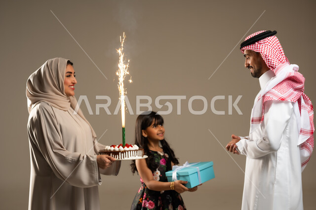 الألفة والمودة بين أفراد الأسرة السعودية, ايماءات البهجة والسرور, الاجتماعات والاحتفالات العائلية، بورتريه مقرب لعائلة عربية خليجية سعودية يحتفلون بعيد ميلاد الأب ويقدمون له قالب الكيك المزين والهدايا، خلفية بيج