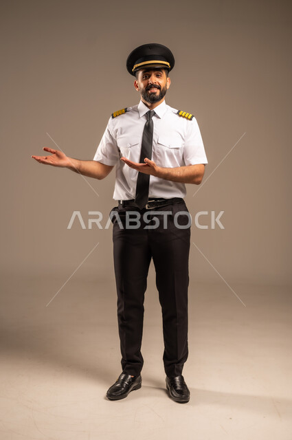  طاقم الاستقبال والترحيب بالركاب، العمل في مجال الطيران، مفهوم السياحة والسفر، رحلات جوية سياحية, خطوط الطيران السعودية,  بورتريه لكابتن طيار عربي سعودي خليجي مبتسم يرتدي الزي الرسمي يشير بيديه الى الجانب بتعابير السعادة والسرور، الجسم بالطول الكامل, خلفية رمادية