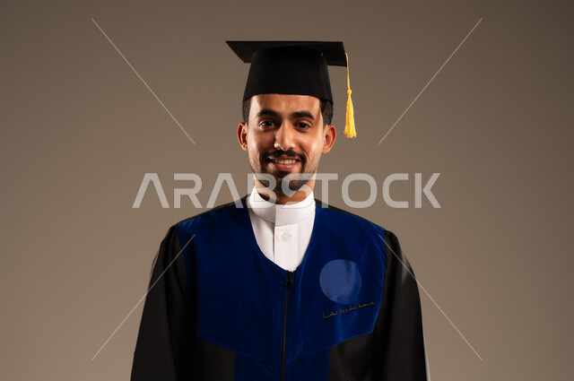  مفهوم الاجتهاد والتفوق، الشعور بالفرح والفخر والثقة بالنفس, الاحتفال بإنهاء الدراسة الجامعية، بورتريه مقرب لطالب عربي سعودي خليجي يرتدي العباءه وقبعة التخرج ينظر الى الكاميرا بإيماءات الرضا والسرور, خلفية بنية 