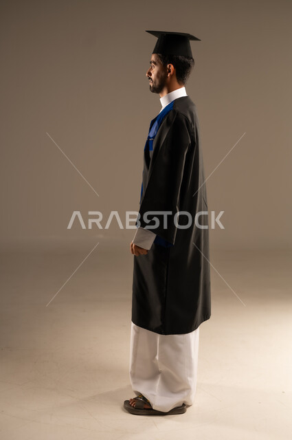  الشعور بالفرح والفخر والثقة بالنفس, مفهوم الاجتهاد والتفوق، الاحتفال بإنهاء الدراسة الجامعية، بورتريه من الجانب لطالب عربي سعودي خليجي يرتدي العباءه وقبعة التخرج ينظر إلى الكاميرا بإيماءات الرضا والسرور, صورة الجسم بالطول الكامل, خلفية بنية 