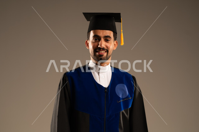  الشعور بالفرح والفخر والثقة بالنفس, مفهوم الاجتهاد والتفوق، الاحتفال بإنهاء الدراسة الجامعية، بورتريه مقرب لطالب عربي سعودي خليجي يرتدي العباءه وقبعة التخرج ينظر إلى الكاميرا بإيماءات الرضا والسرور, خلفية بنية 