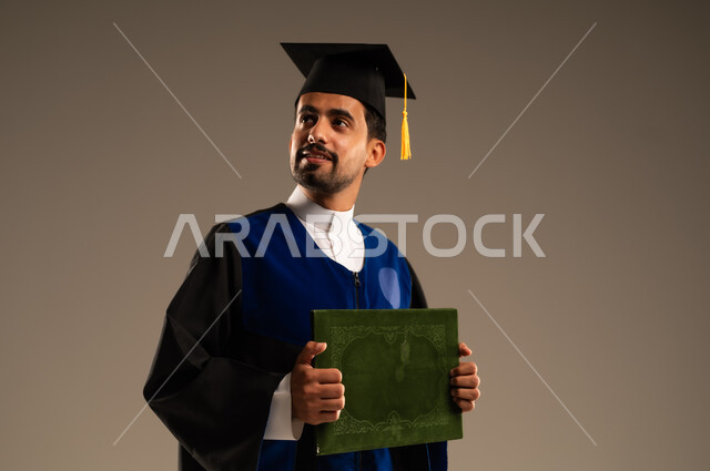 الاحتفال بإنهاء الدراسة الجامعية، بورتريه مقرب لطالب عربي سعودي خليجي يرتدي العباءه وقبعة التخرج ينظر إلى شيء ما يحمل بيده الاطروحة بإيماءات الرضا والسرور, الشعور بالفرح والفخر والثقة بالنفس, مفهوم الاجتهاد والتفوق، خلفية بنية