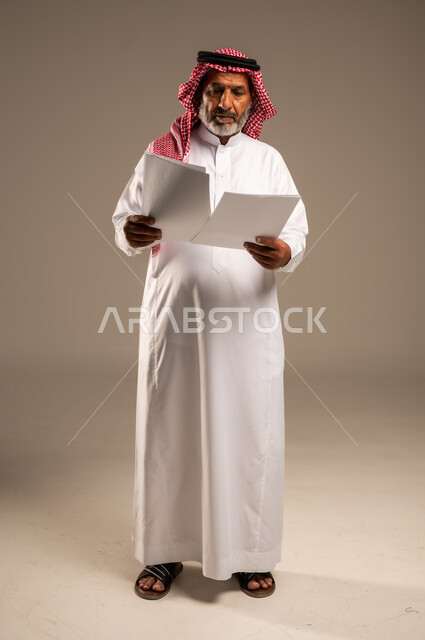 متابعة المراسلات والسجلات، بورتريه لرجل مسن عربي خليجي سعودي يرتدي العباءة والشماغ مبتسم يحمل بيديه اوراق بيضاء و ينظر اليهم، انجاز المهام المطلوبة, الطول الكامل للجسم، خلفية بنية 