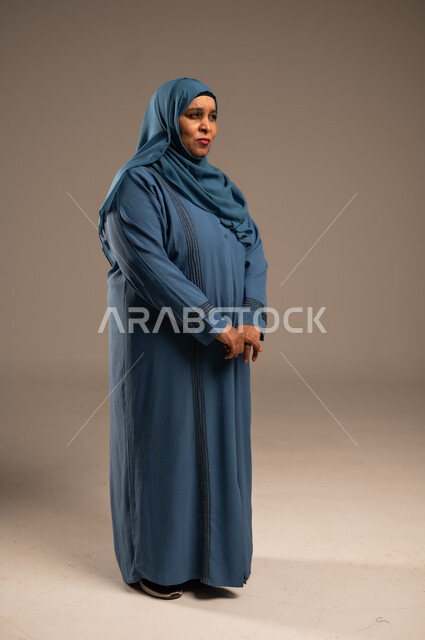 الشعور بالخيبة والانزعاج، الندم على شيء ما، بورتربه لسيدة عربية سعودية خليجية كبيرة بالسن ترتدي العباءة والحجاب, إيماءات تدل على الحزن والإحباط، الجسم بالطول الكامل، خلفية بيج