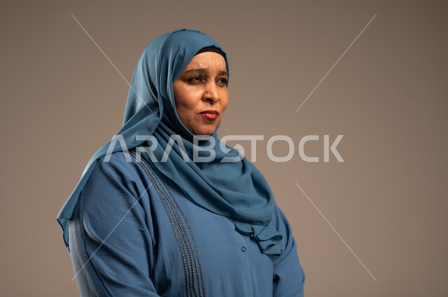  الشعور بالخيبة والانزعاج، الندم على شيء ما، بورتربه مقرب لسيدة عربية سعودية خليجية كبيرة بالسن ترتدي العباءة والحجاب, إيماءات تدل على الحزن والإحباط، خلفية بيج 