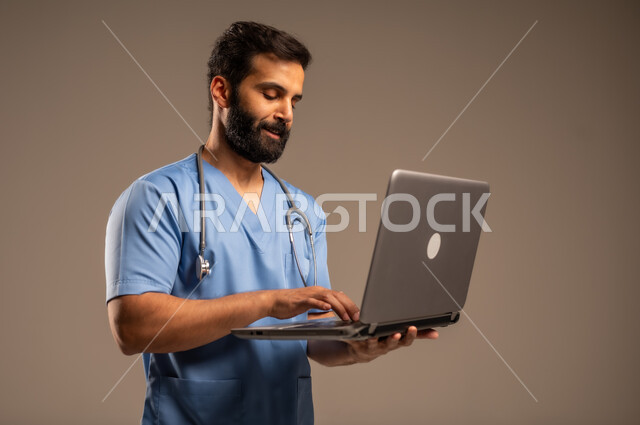 دمج التكنولوجيا مع الطب، الاستعداد لتقديم الخدمات والرعاية الصحية بكل كفاءة، بورتريه مقرب لممرض عربي خليجي سعودي يرتدي اليونيفورم الخاص بالعمل يستخدم الحاسوب المحمول، استخدام الأجهزة التقنية الحديثة، خلفية بيج