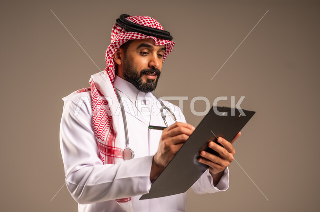 دراسة الحالات المرضية، بورتريه مقرب لطبيب عربي خليجي سعودي يرتدي الثوب التقليدي والشماغ والمعطف الأبيض يمسك بيده ملفات المرضى يقوم بتدوين البيانات، مهن ووظائف طبية في المملكة العربية السعودية، تقديم الاستشارات والرعاية الصحية بكل كفاءة، خلفية بيج
