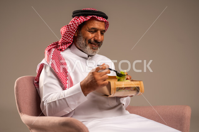 توفير العناصر الغذائية الضرورية للجسم، تناول وجبات الطعام الصحية، بورتريه لرجل مسن عربي خليجي سعودي يرتدي زي تقليدي وشماغ يجلس على كرسي يحمل بيده طبق، الحفاظ على الرشاقة والصحة البدنية، خلفية بيج