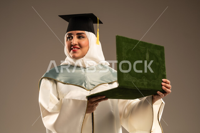أهمية الدراسة الجامعية والفرح بتحقيق النجاح, ايماءات البهجة والسعادة بالوصول لحلم التخرج، بورتريه مقرب لخريجة عربية سعودية خليجية محجبة ترتدي العباءة البيضاء وقبعة التخرج تمسك بيدها شهادة التفوق, خلفية بيج