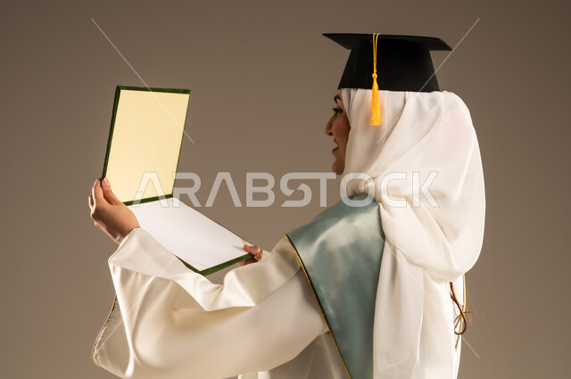 أهمية الدراسة الجامعية والفرح بتحقيق النجاح, ايماءات البهجة والسعادة بالوصول لحلم التخرج، بورتريه مقرب لخريجة عربية سعودية خليجية محجبة ترتدي العباءة البيضاء وقبعة التخرج تمسك بيدها شهادة التفوق, خلفية بيج