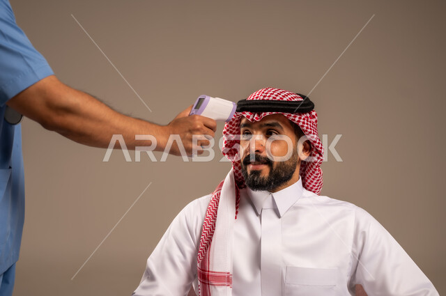 الحاجة إلى المساعدة الطبية، ممرض يقوم بقياس درجة حرارة الجسم بواسطة جهاز الترمومتر الرقمي، شركات التمريض المنزلي في المملكة العربية السعودية، بورتريه مقرب لرجل عربي خليجي سعودي يرتدي الثوب التقليدي والشماغ يقوم بالاطمئنان على حالته الصحية، خلفية بيج