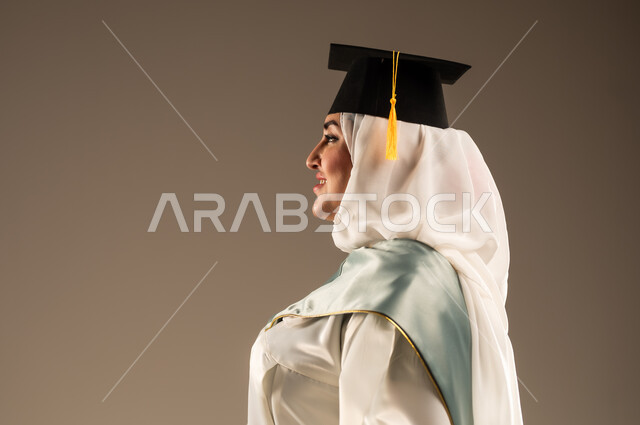 ايماءات البهجة والسعادة بالوصول لحلم النجاح, الاحتفال بإنهاء الدراسة الجامعية، بورتريه مقرب من الجانب لخريجة عربية سعودية خليجية محجبة ترتدي العباءة البيضاء وقبعه التخرج تنظر الى شيء ما, خلفية بيج